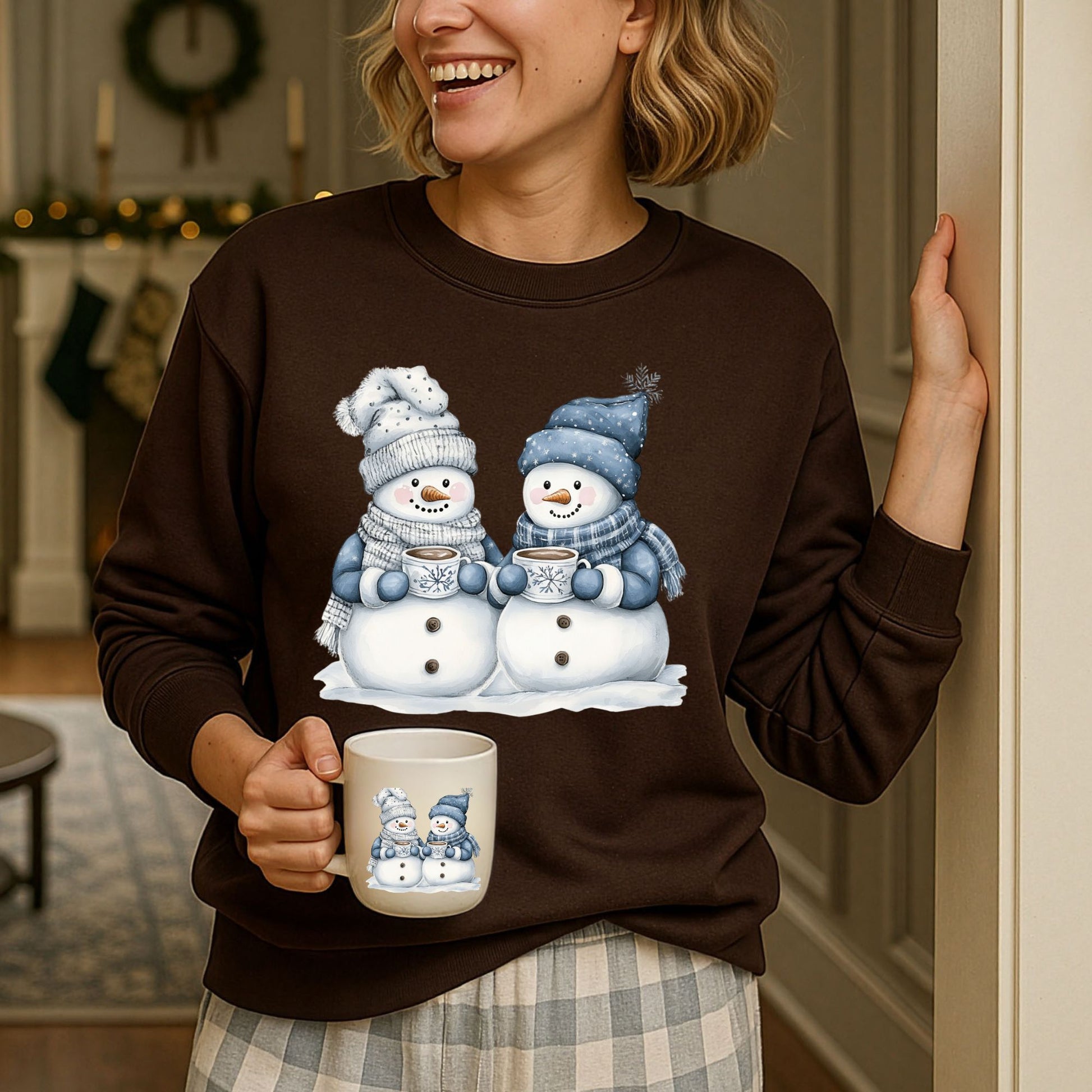 Woman in a brown sweatshirt with two snowpeople in blue hats and scarves holding hot chocolate.