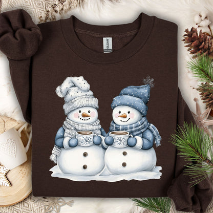 Dark Chocolate heavy blend sweatshirt with two snowpeople in blue hats and scarves holding hot chocolate.