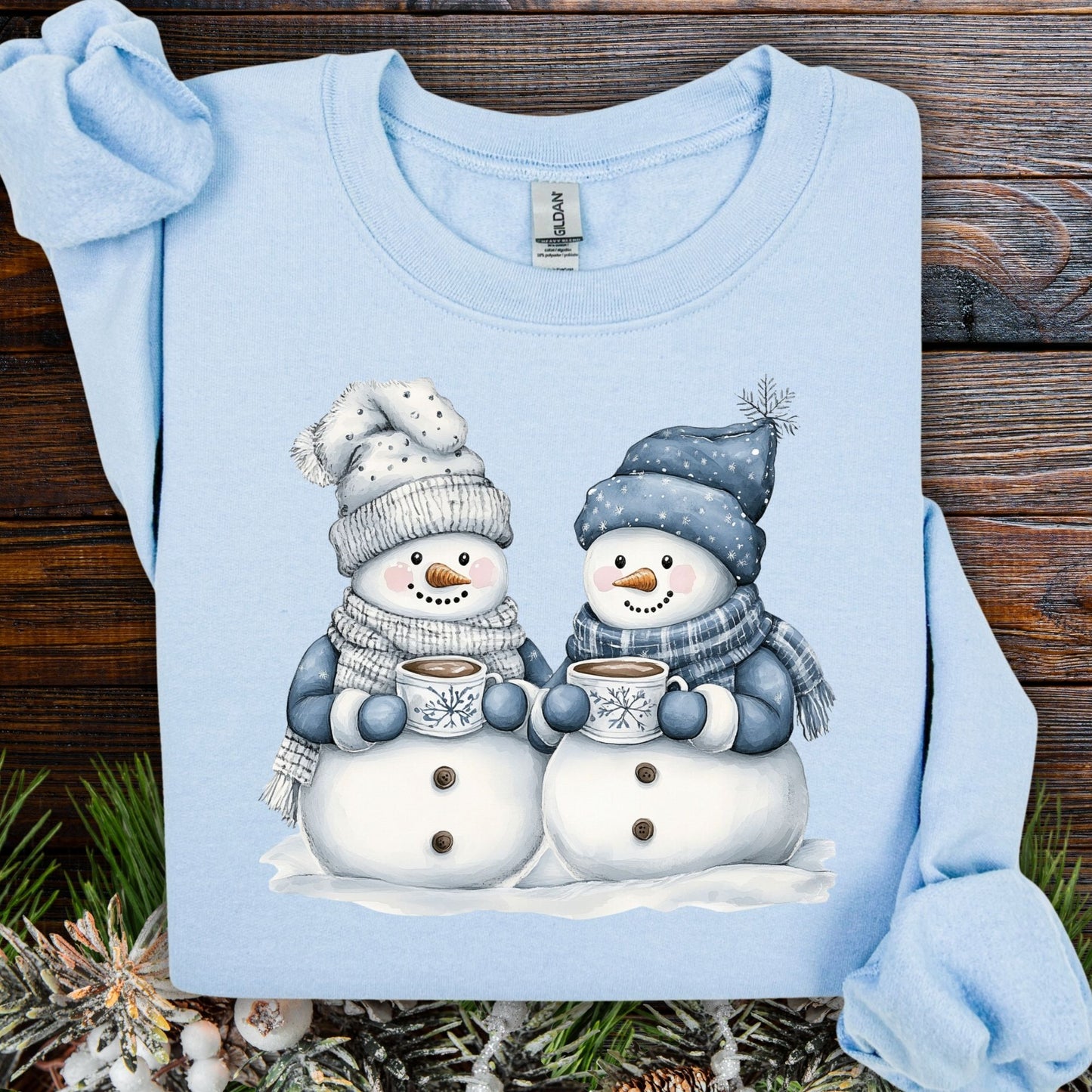 Light blue heavy blend sweatshirt with two snowpeople in blue hats and scarves, holding hot chocolate.