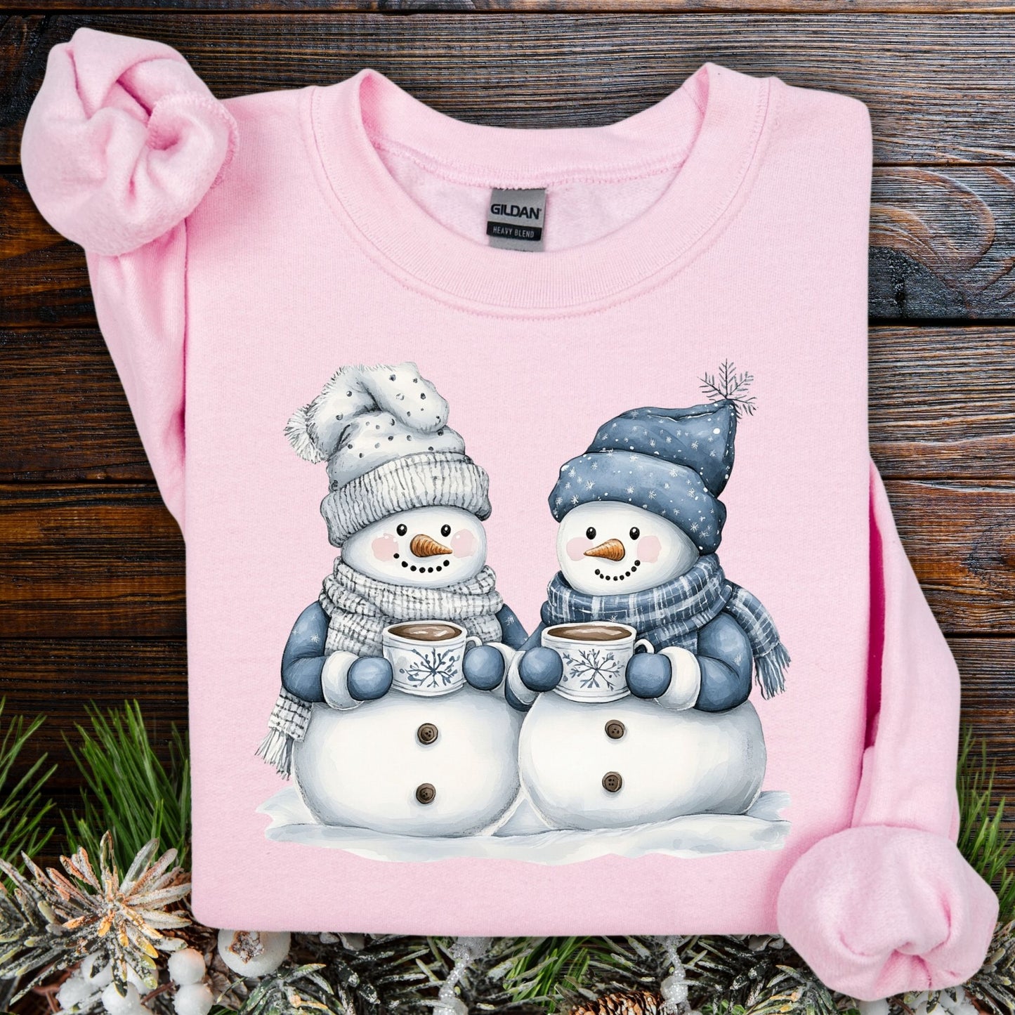 Light pink Gildan heavy blend sweatshirt with two snowpeople in blue hats holding hot chocolate.