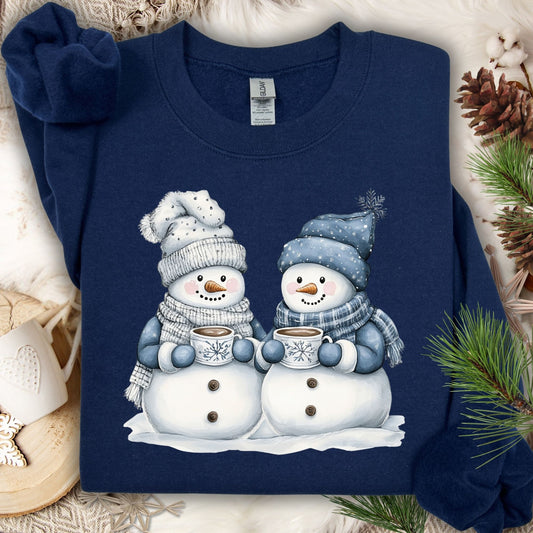 Navy heavy blend sweatshirt with two snowpeople in blue hats and scarves holding hot chocolate.