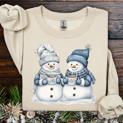 Sand heavy blend sweatshirt with two snowmen in blue hats, mittens, and scarves holding hot chocolate.