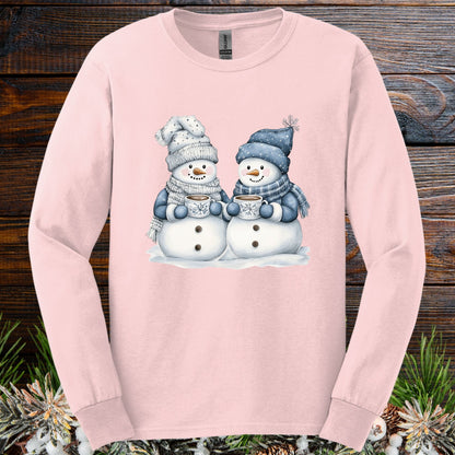 Light pink long-sleeve tee with two cozy snowmen holding hot chocolate, in soft blues and warm grays.