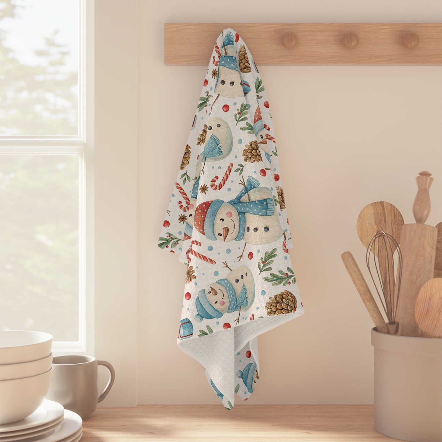 Microfiber tea towel with snowmen, candy canes, pine cones, and holly, hanging on a wooden hook.