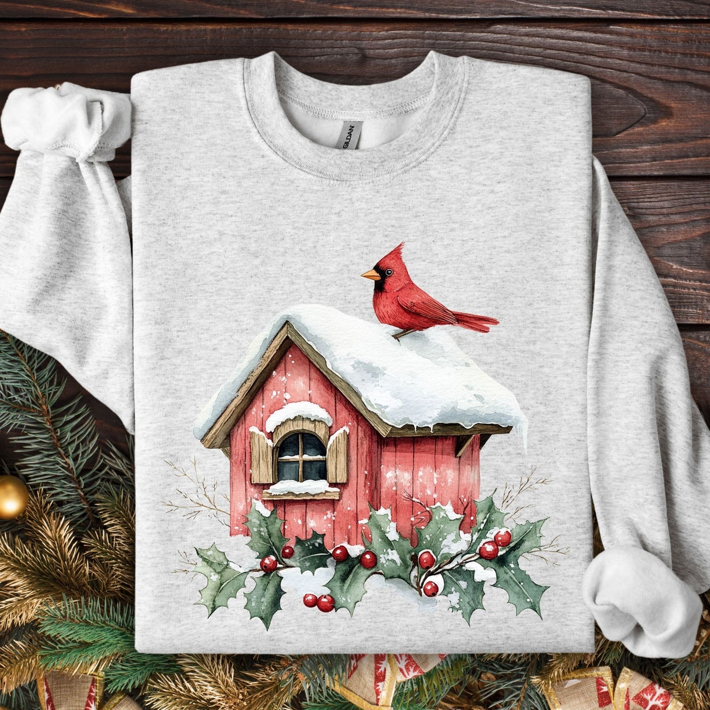 Ash Gildan sweatshirt with a watercolor red cardinal on a snow-covered birdhouse with holly.
