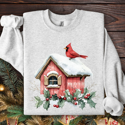 Ash Gildan sweatshirt with a watercolor red cardinal on a snow-covered birdhouse with holly.
