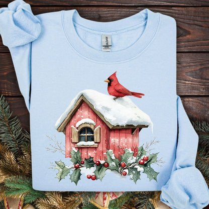 Light blue Gildan sweatshirt with a watercolor red cardinal on a snow-covered birdhouse, holly, and berries.