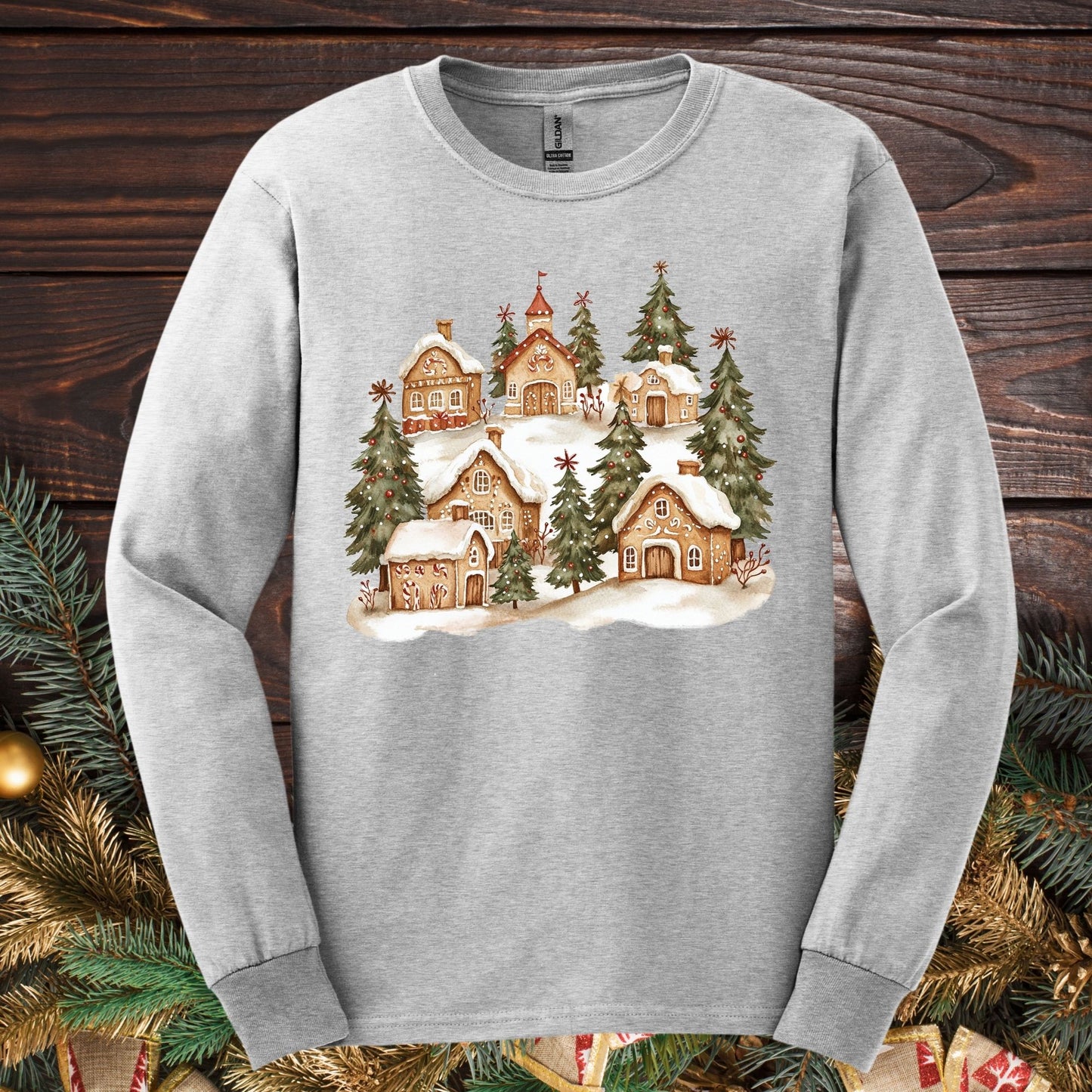 Ash gray long sleeve tee with a watercolor snowy gingerbread village and evergreens.