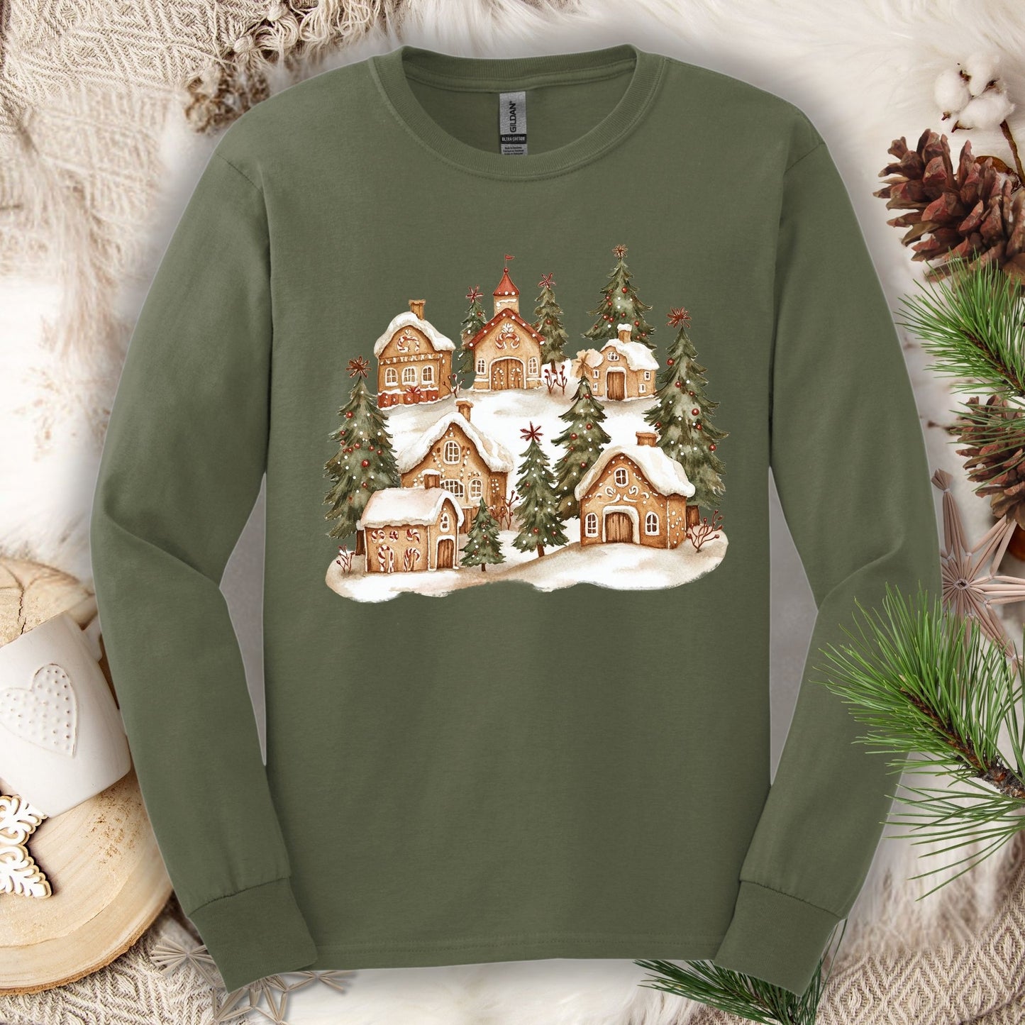Military Green long sleeve tee with a watercolor snowy gingerbread village and evergreen trees.