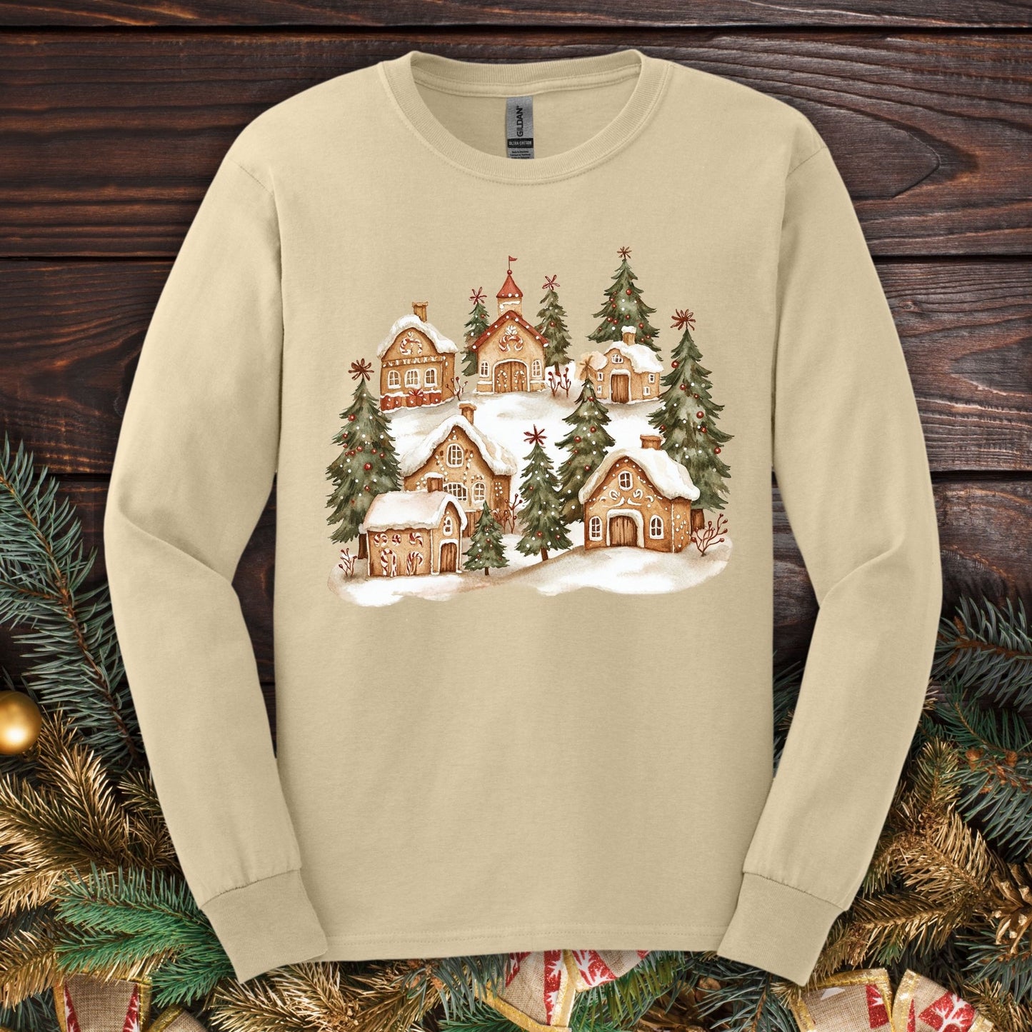 Sand long sleeve tee with a watercolor snowy gingerbread village and evergreens.