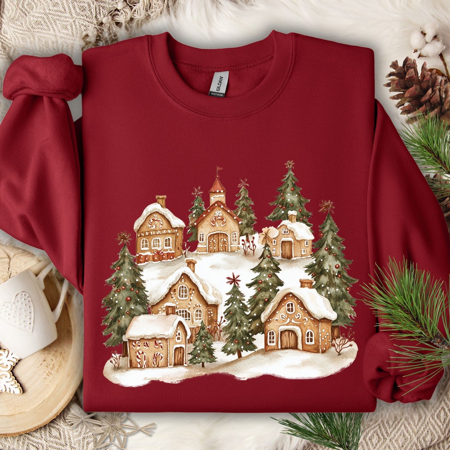 Cardinal Red Gildan 18000 sweatshirt with a watercolor snowy gingerbread village and evergreen trees.