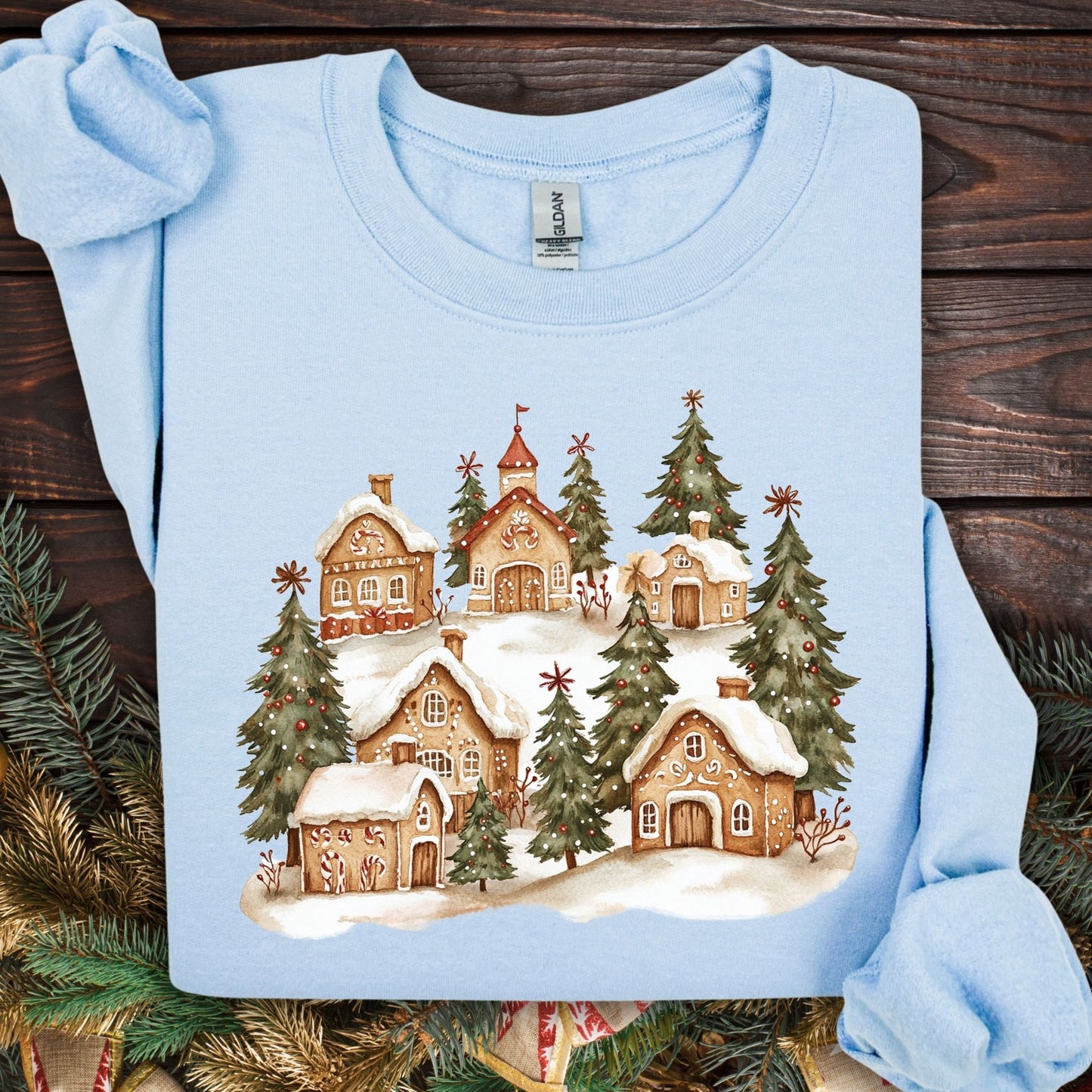 Light blue Gildan 18000 sweatshirt with a watercolor snowy gingerbread village and evergreen trees.