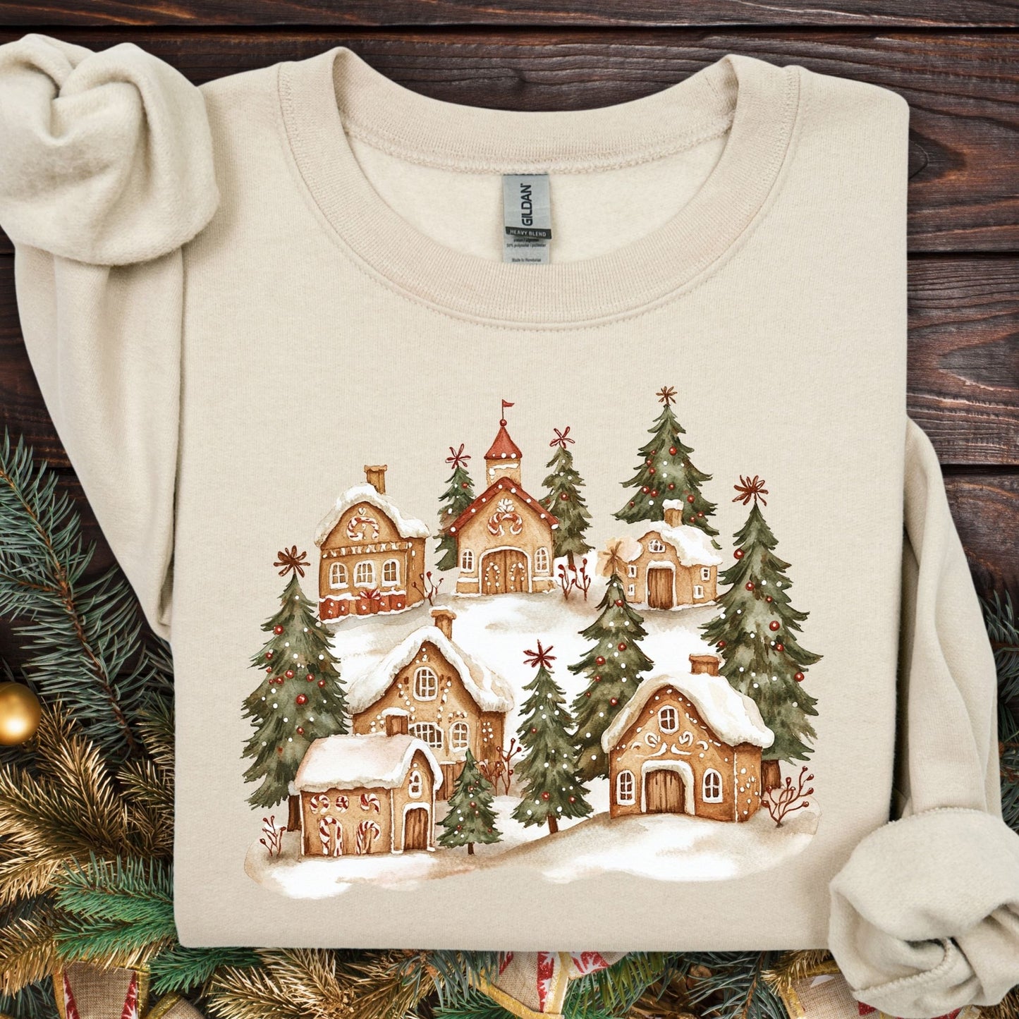 Sand Gildan 18000 sweatshirt with a watercolor snowy gingerbread village and evergreen trees.