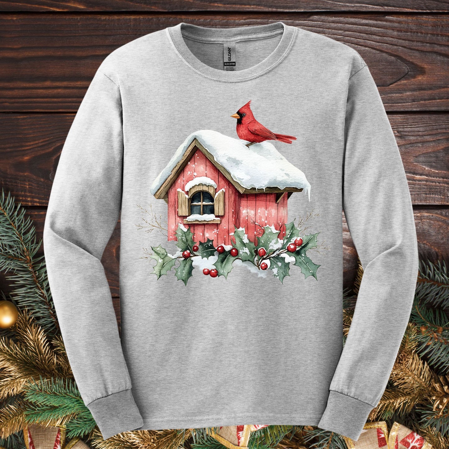 Ash gray Gildan Softstyle long sleeve tee with a watercolor red cardinal on a snowy rustic birdhouse, holly, and berries.