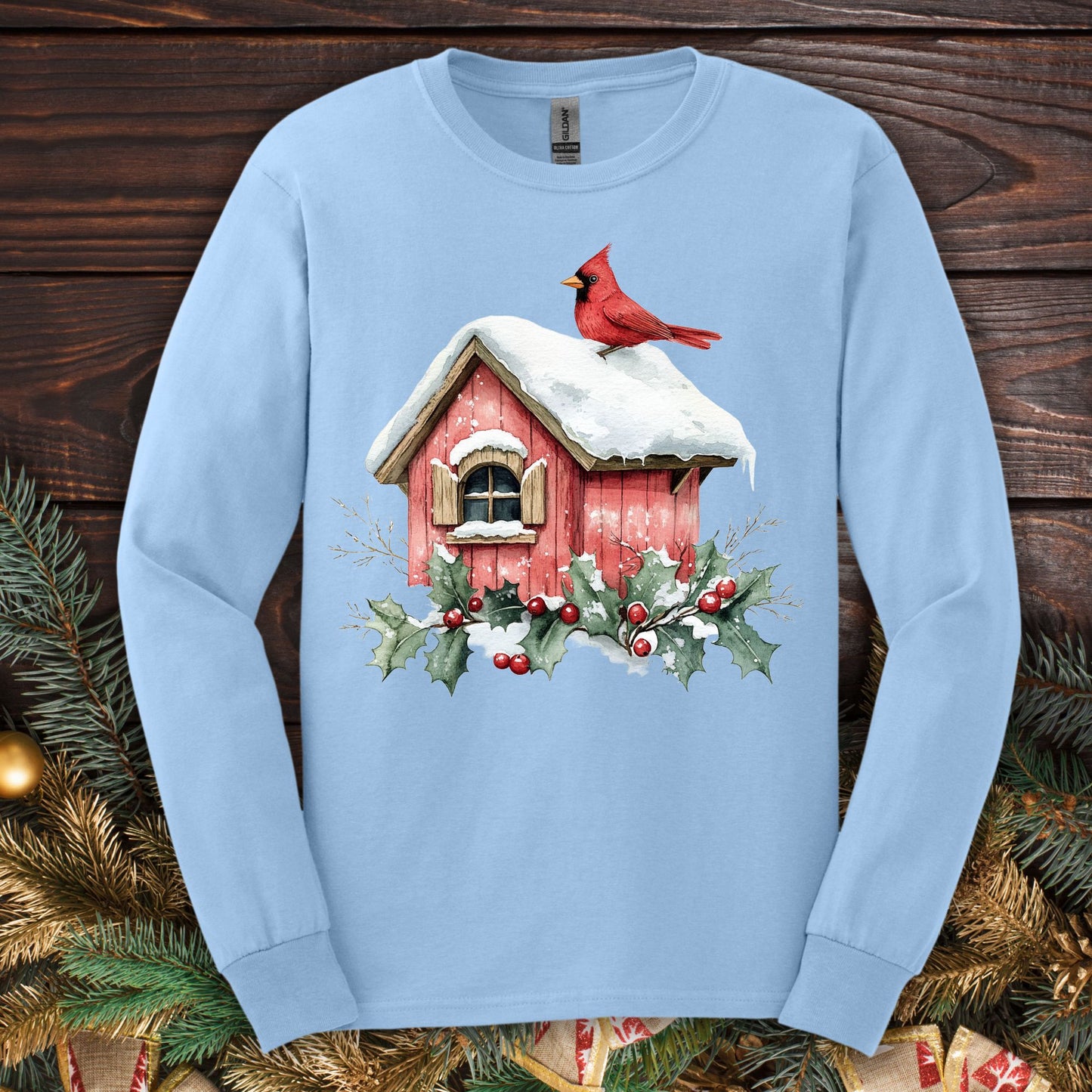 Light blue long sleeve tee with a watercolor red cardinal on a snowy rustic birdhouse with holly.