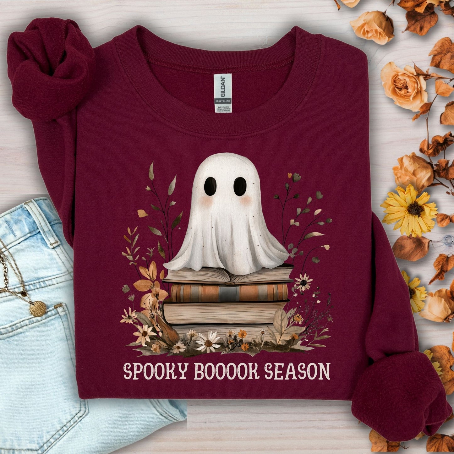 Maroon Gildan sweatshirt with a boho ghost on vintage books, surrounded by autumn wildflowers and "Spooky Booook Season" text.