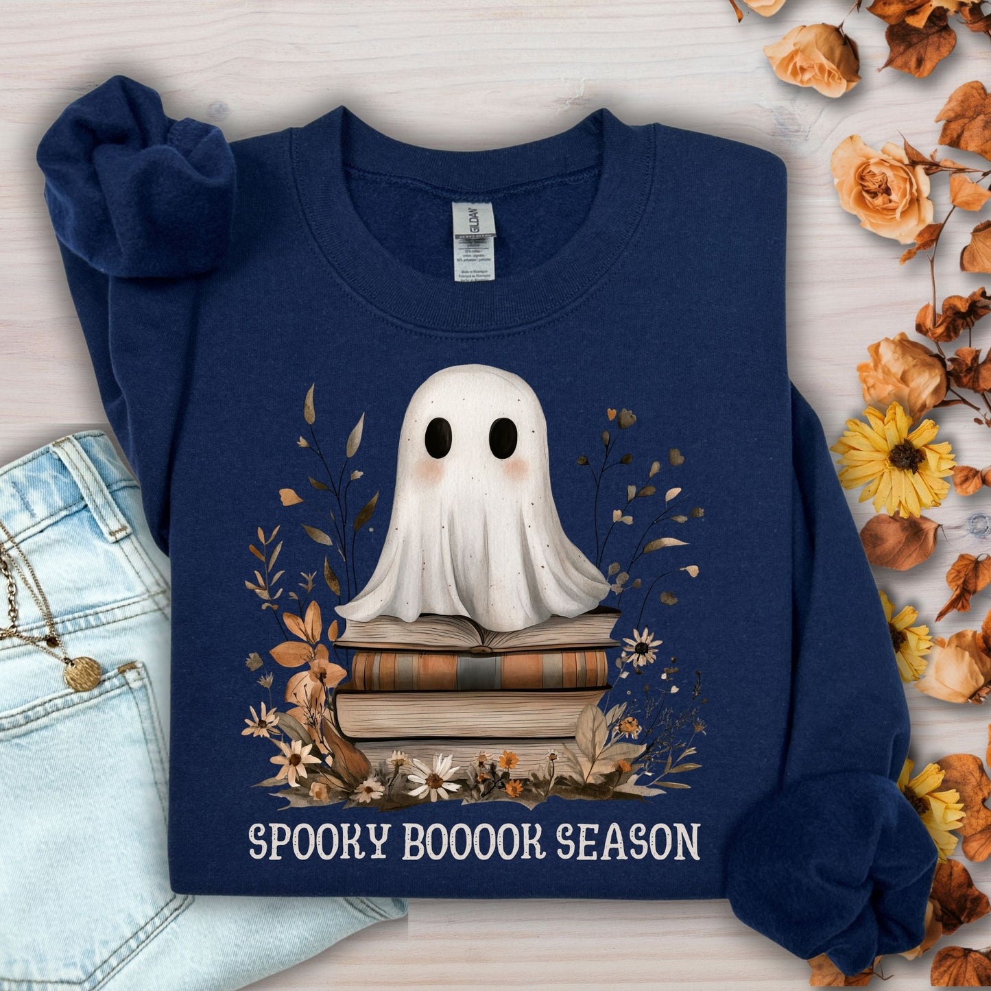 Navy Gildan sweatshirt with a boho ghost on vintage books, surrounded by autumn wildflowers and "SPOOKY BOOOOK SEASON" text.