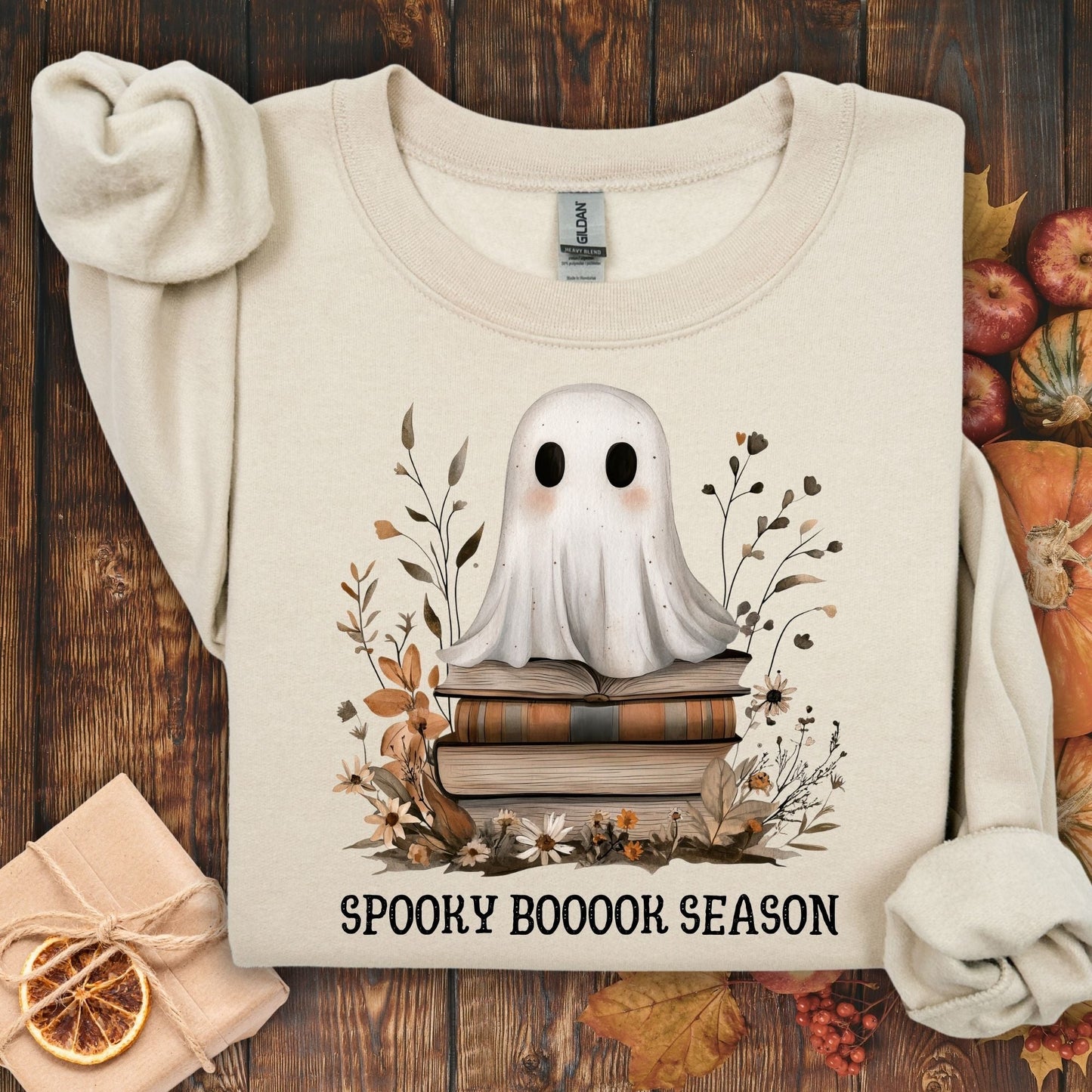 Sand Gildan crewneck sweatshirt with a boho ghost on vintage books, autumn wildflowers, and "SPOOKY BOOOOK SEASON.