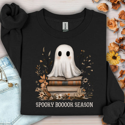 Black Gildan sweatshirt with a boho ghost on vintage books, surrounded by autumn wildflowers and "Spooky Booook Season" text.