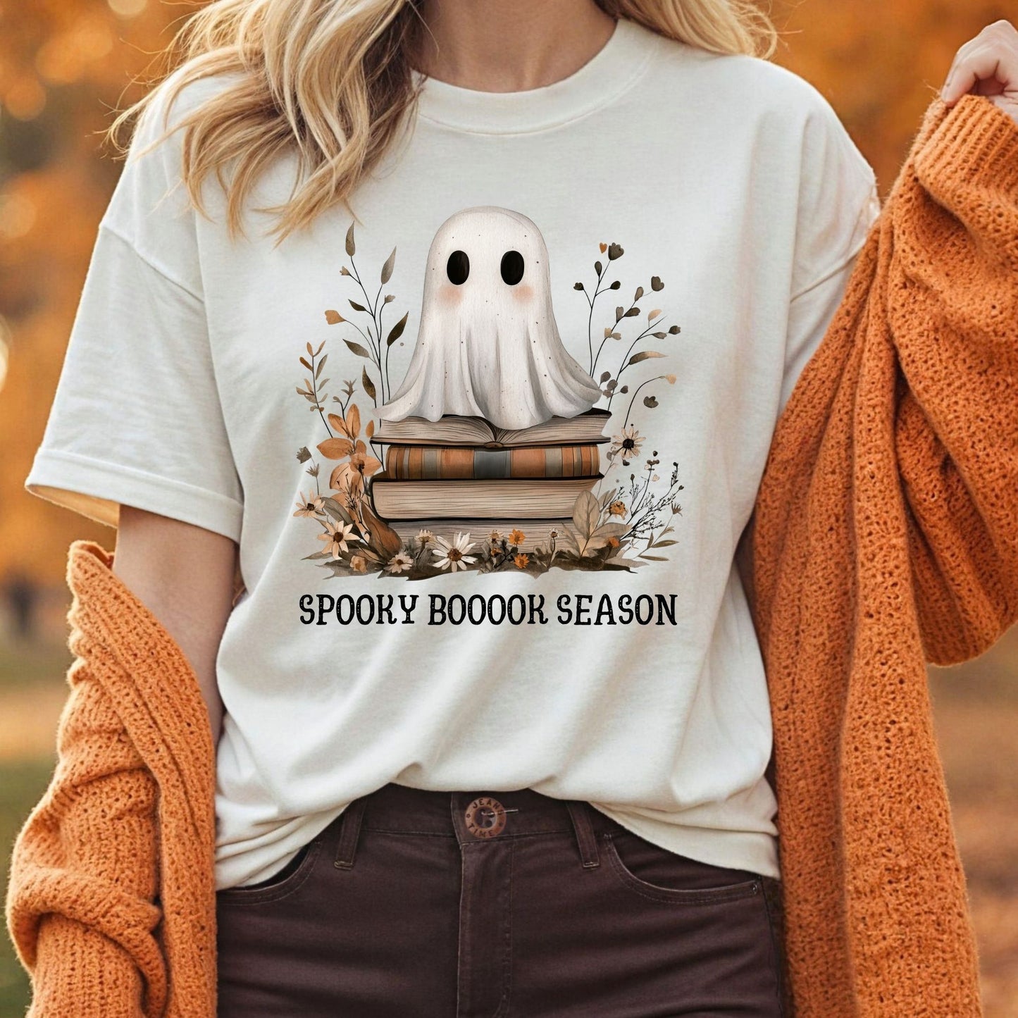 White tee with a whimsical ghost on vintage books, surrounded by fall foliage, and "SPOOKY BOOOOK SEASON" text.