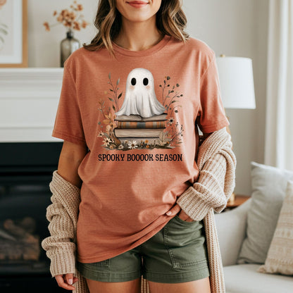 Burnt orange "Spooky Boooook Season" tee with a ghost on books, worn by a woman with a cardigan.