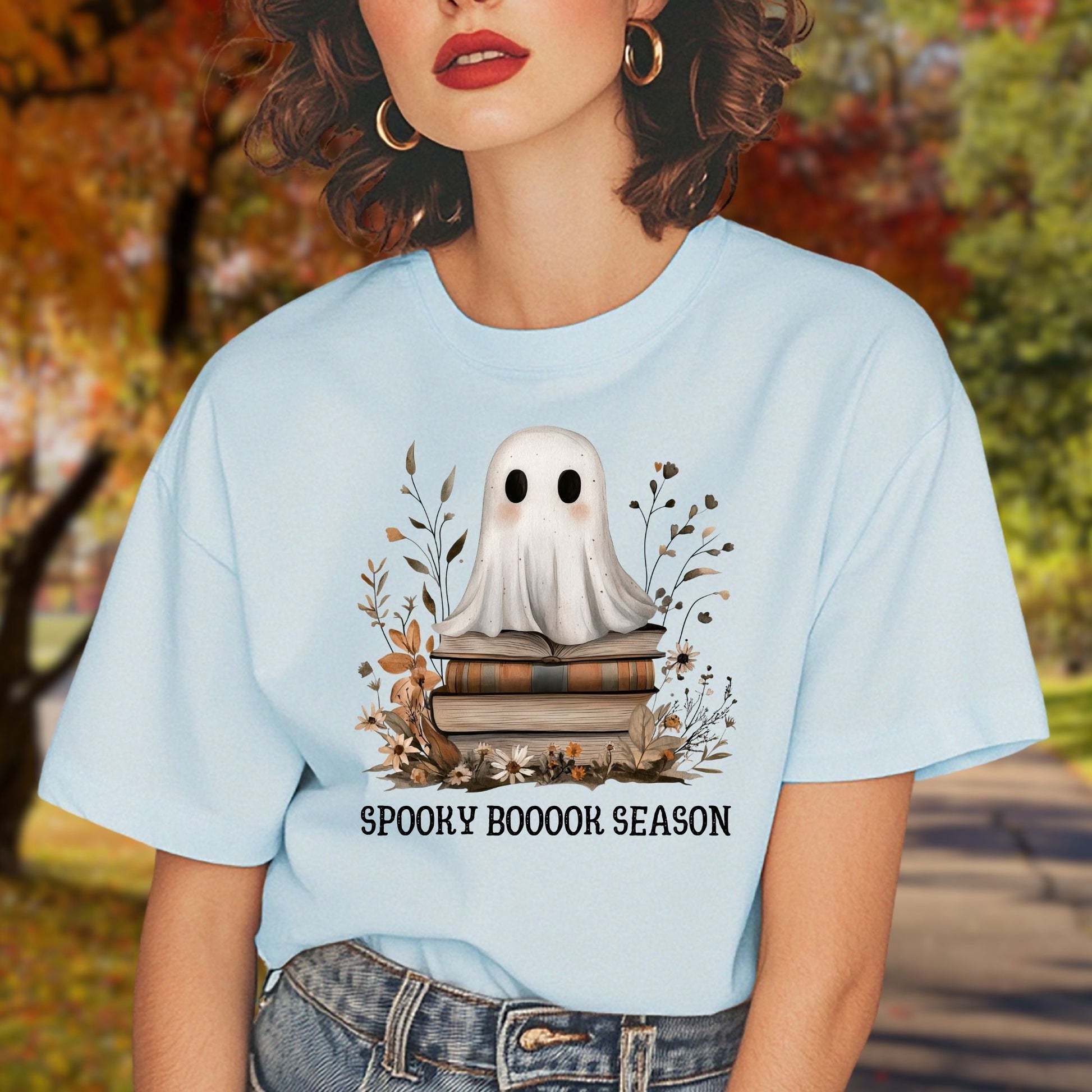 Light blue tee with a whimsical ghost on vintage books, surrounded by fall foliage, text "SPOOKY BOOOOK SEASON".