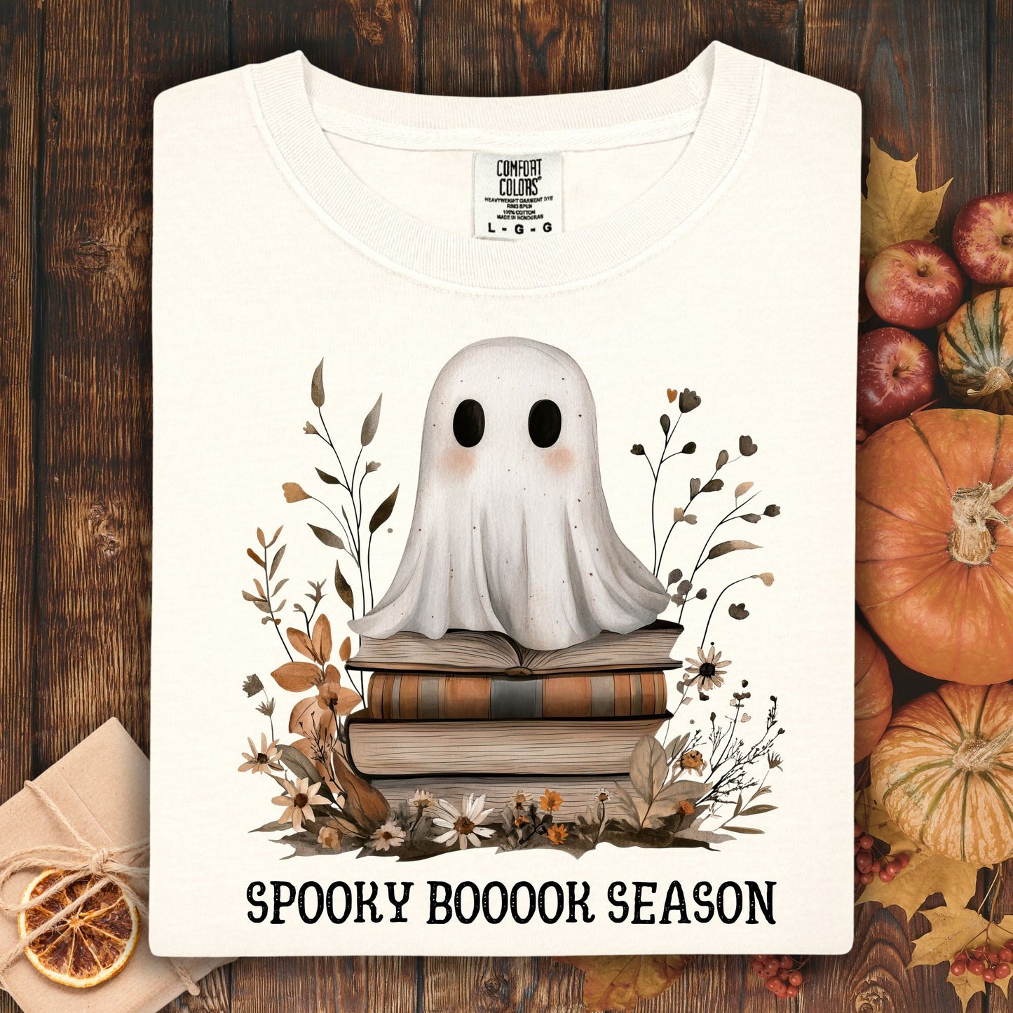 Ivory Comfort Colors tee with a cute ghost on vintage books, surrounded by autumn foliage and "Spooky Boooook Season" text.