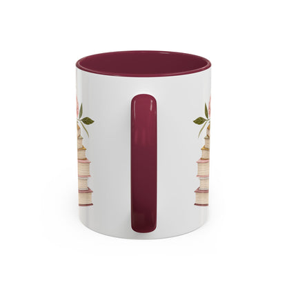White ceramic mug with a burgundy handle and interior, featuring a watercolor stack of books and floral accents.