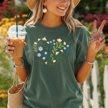 Woman in a dark green t-shirt with a heart-shaped botanical design of wildflowers and leaves.
