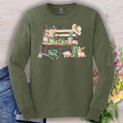 Olive green long sleeve tee with a watercolor garden bench, tools, flowers, and a rabbit design.