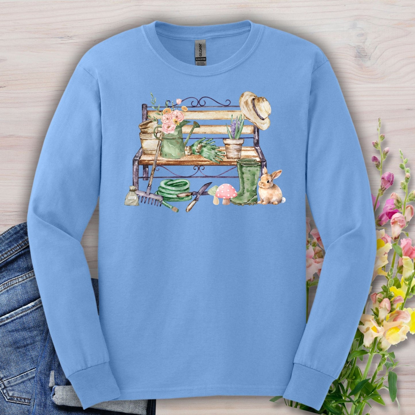 Carolina Blue long sleeve tee with a watercolor garden bench, tools, flowers, and a rabbit.