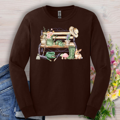 Dark Chocolate long sleeve tee with a watercolor garden bench, tools, flowers, and a rabbit.
