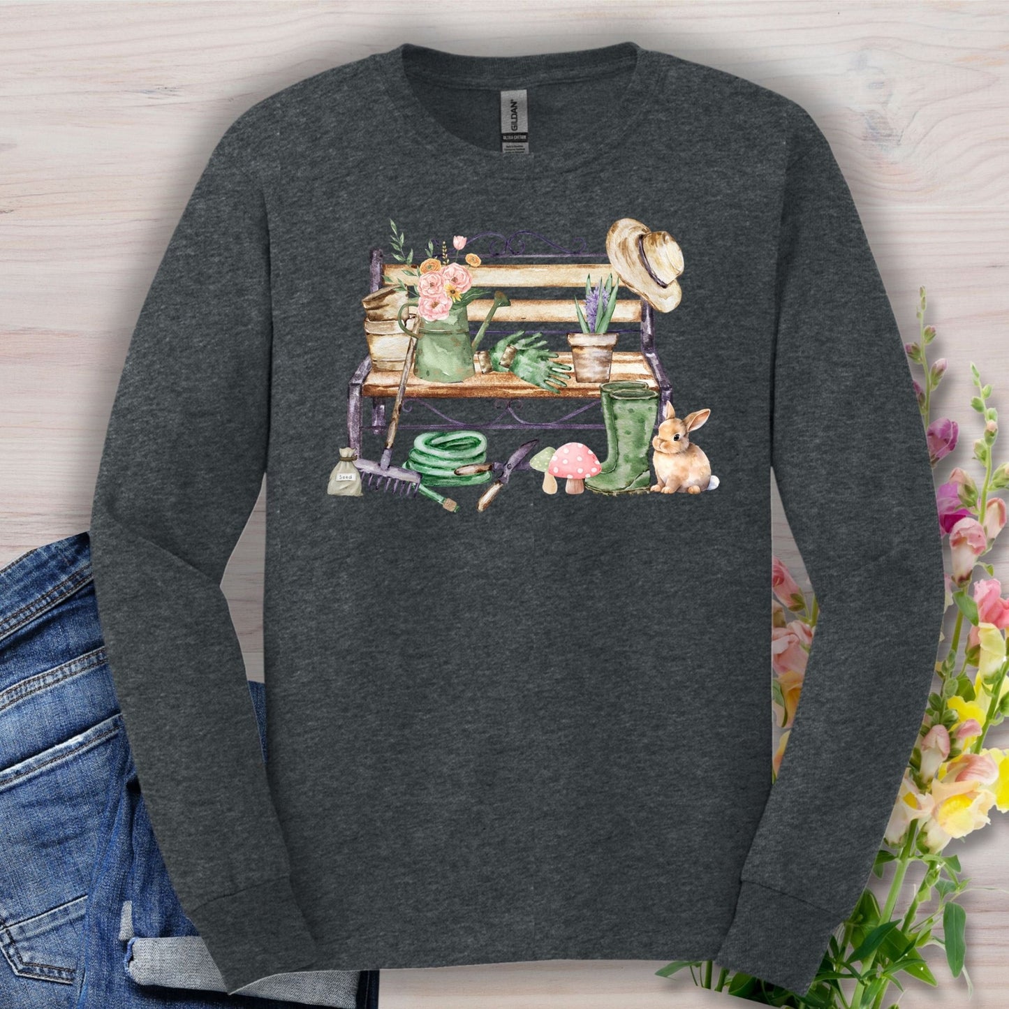 Dark Heather long sleeve tee with a watercolor garden bench, tools, flowers, and a rabbit.