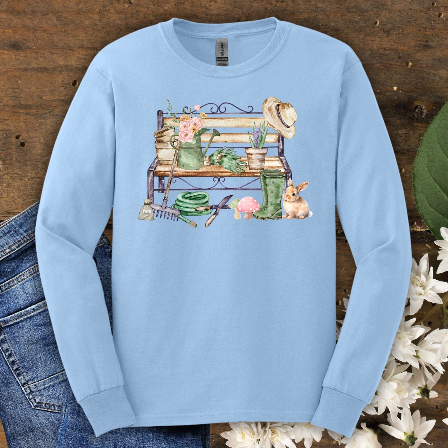 Light blue S long sleeve tee with a watercolor garden bench, tools, flowers, and a rabbit.