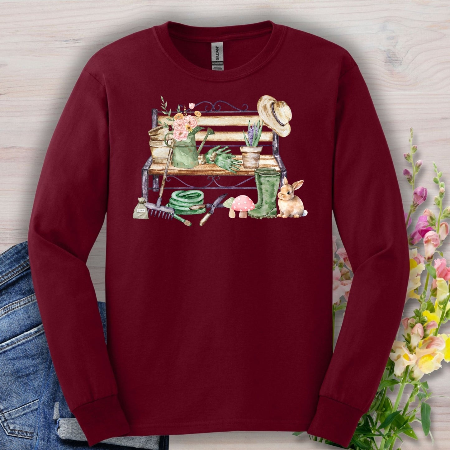 Maroon long-sleeve tee with a watercolor garden bench, tools, flowers, and a rabbit design.