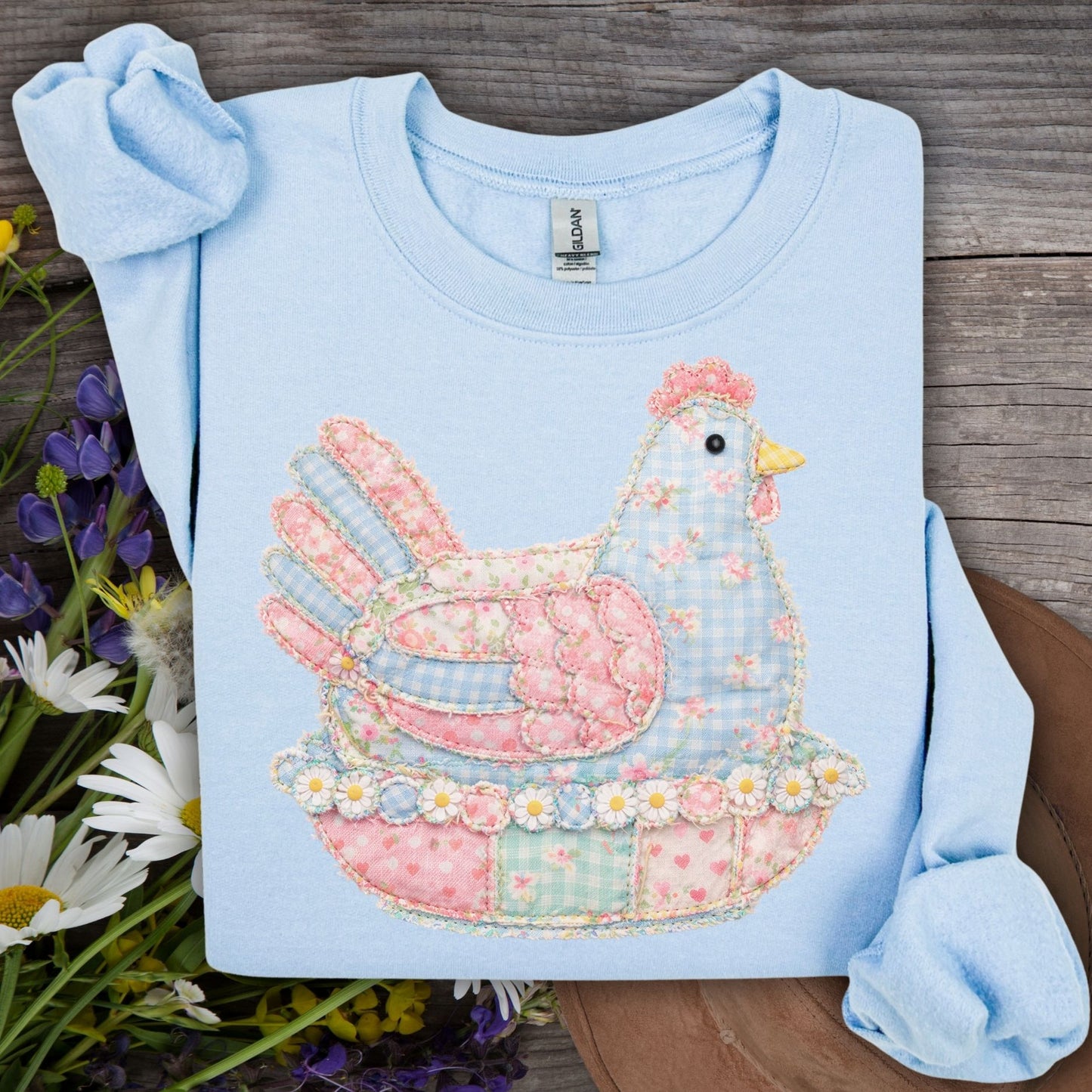 Light blue crewneck sweatshirt with a pastel faux patchwork hen graphic, featuring floral and gingham patterns.