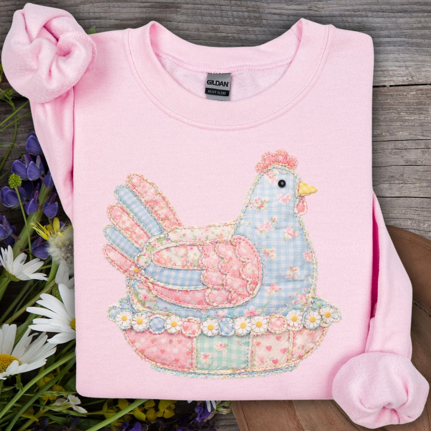 Light pink Gildan sweatshirt with a faux patchwork pastel hen graphic, surrounded by wildflowers.