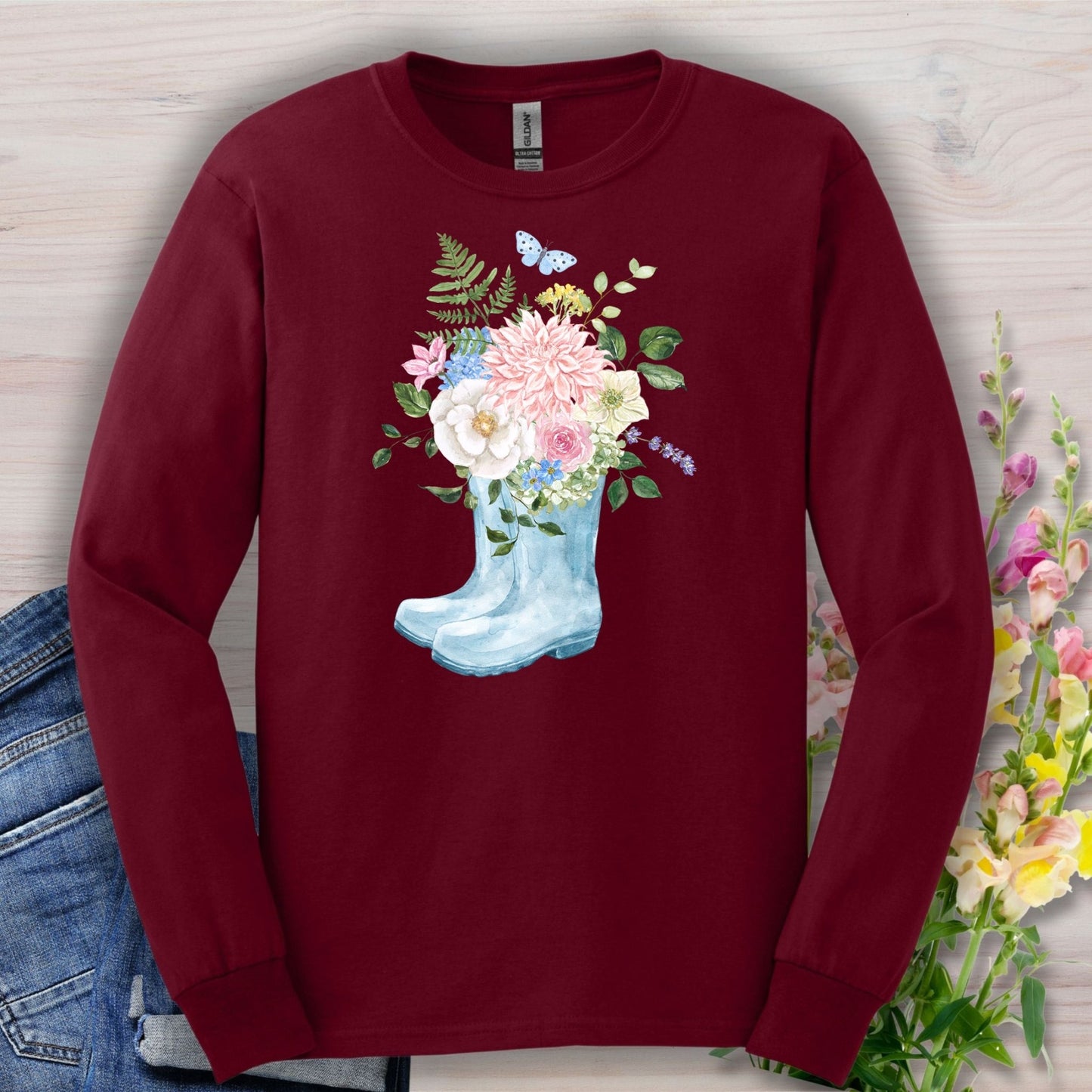 Maroon long-sleeve tee with a watercolor rain boot overflowing with peonies, dahlias, roses, and a butterfly.
