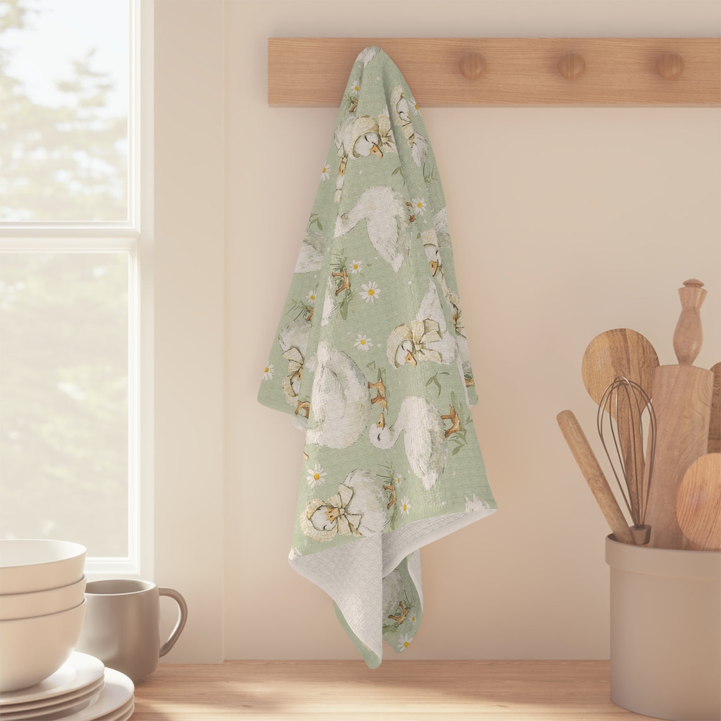 Sage green microfiber tea towel with white ducks and sleepy ducklings, hanging on a wooden peg.