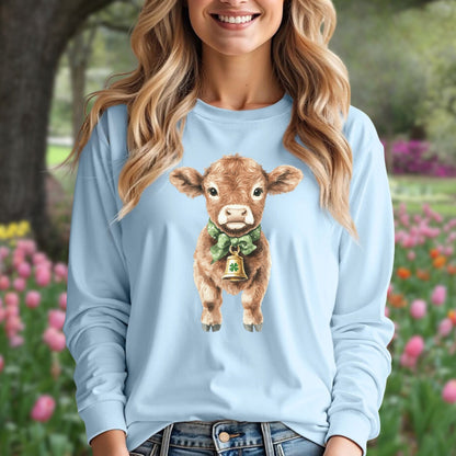 Light blue long-sleeve tee with a watercolor baby Highland cow wearing a green bow and clover bell.