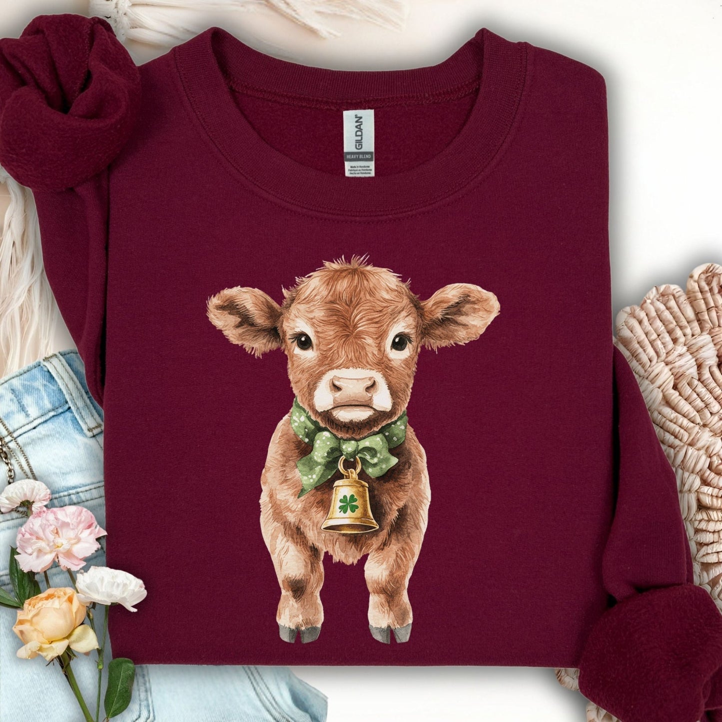Maroon unisex sweatshirt with a watercolor baby Highland cow, green bow, and clover bell.