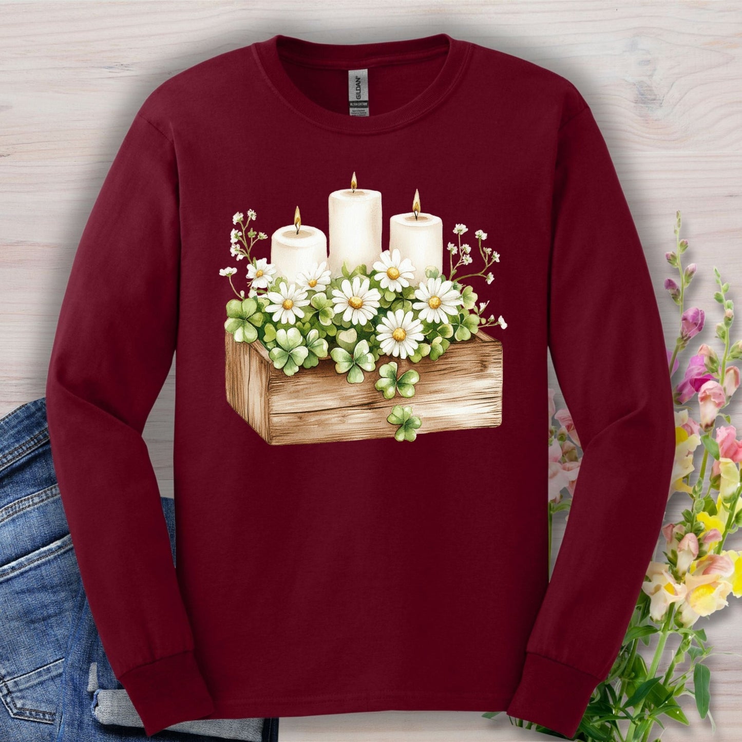 Maroon long sleeve tee with a watercolor clover planter, daisies, and three lit candles.