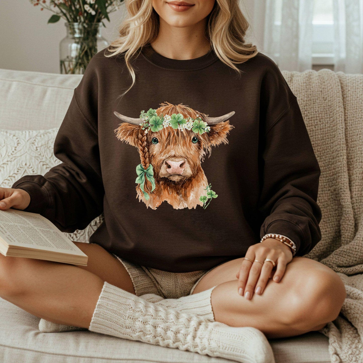 Brown sweatshirt with watercolor Highland cow wearing clover garland and bow.