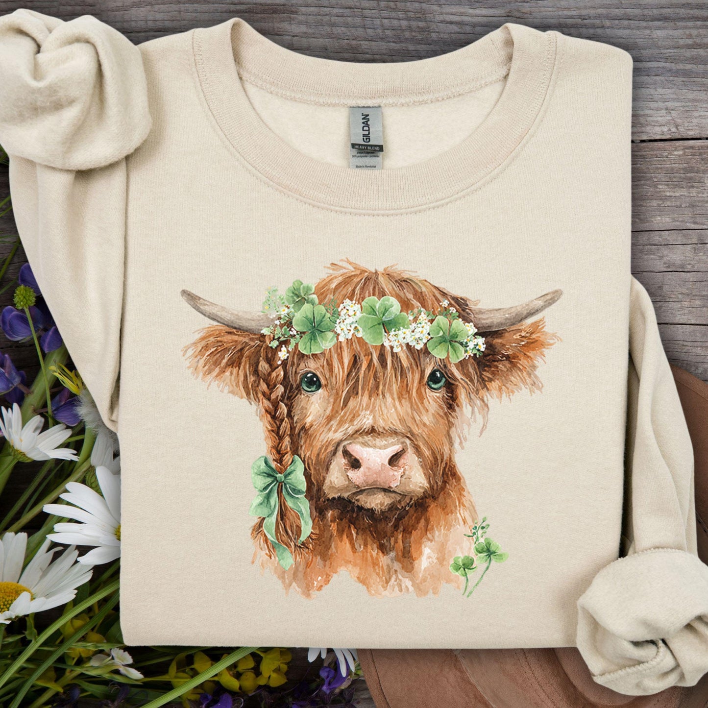Sand sweatshirt with watercolor Highland cow, clover crown, and braided hair with green bow.