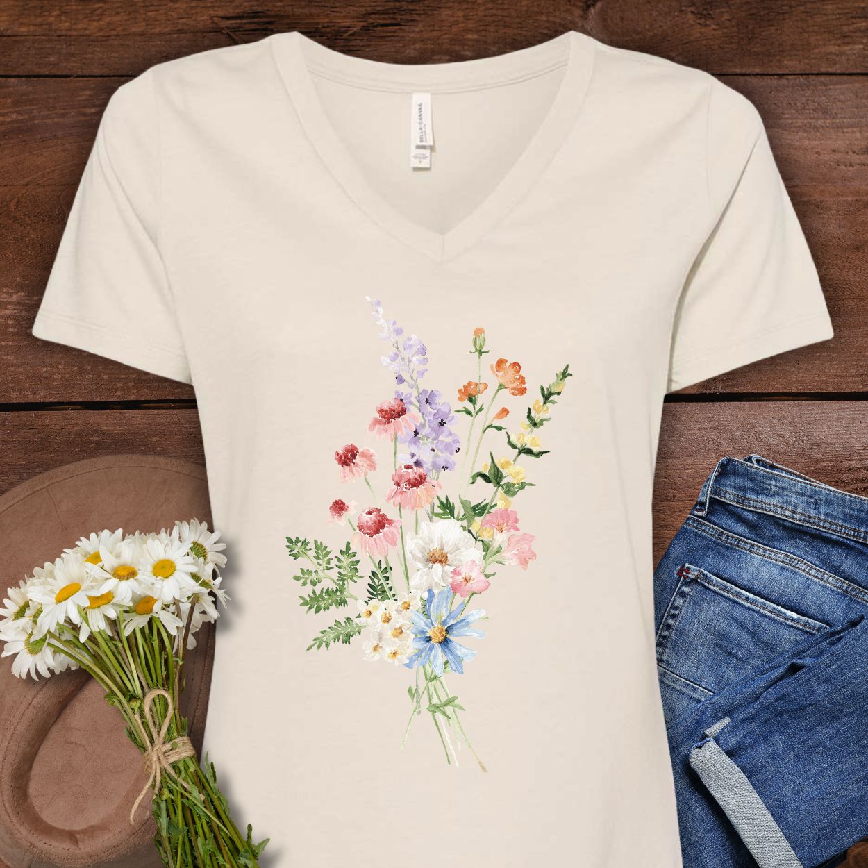 Faded rose v-neck t-shirt with a delicate watercolor wildflower bouquet design, paired with jeans and daisies.