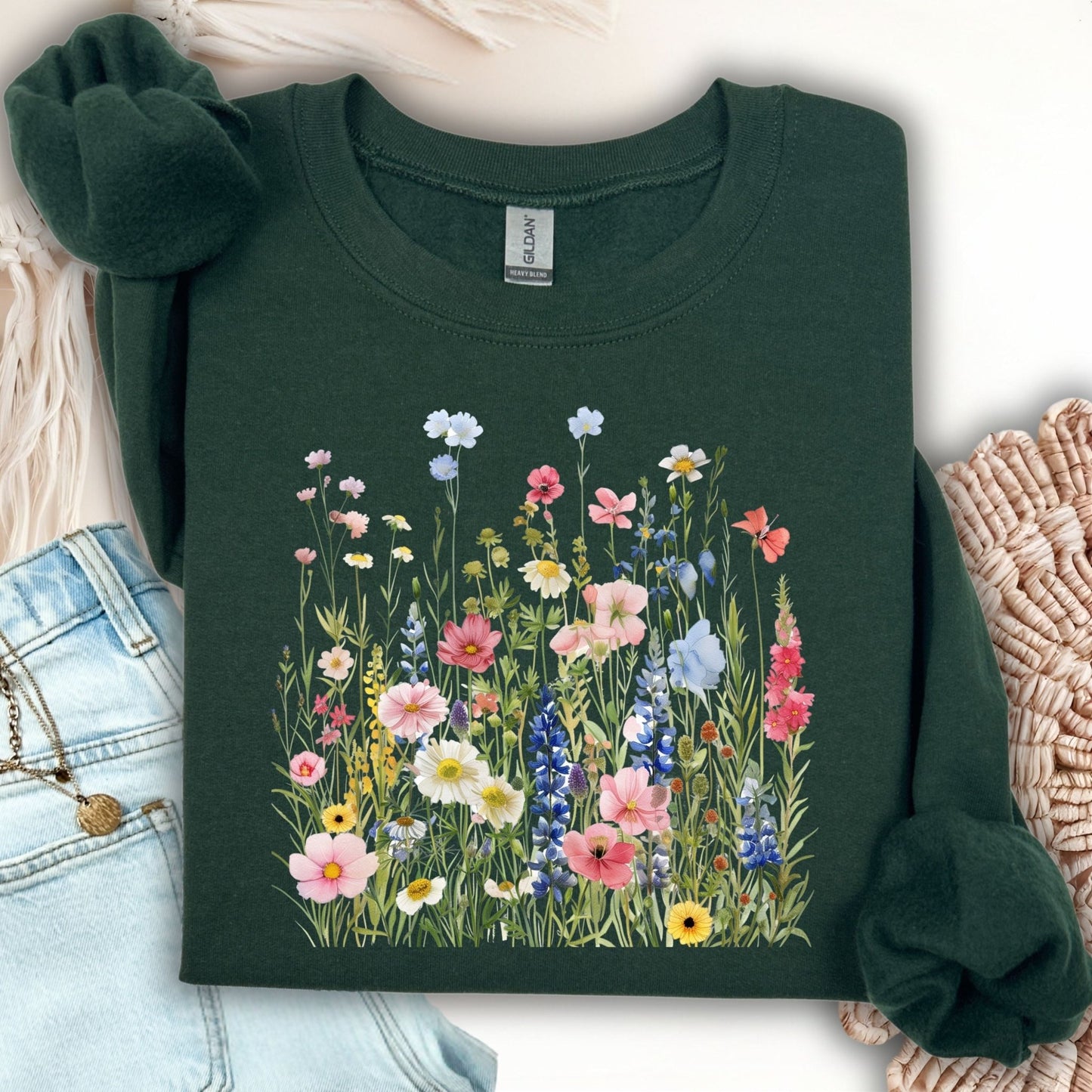 Forest Green Summer Meadow sweatshirt with watercolor wildflowers, folded on a light surface with jeans.
