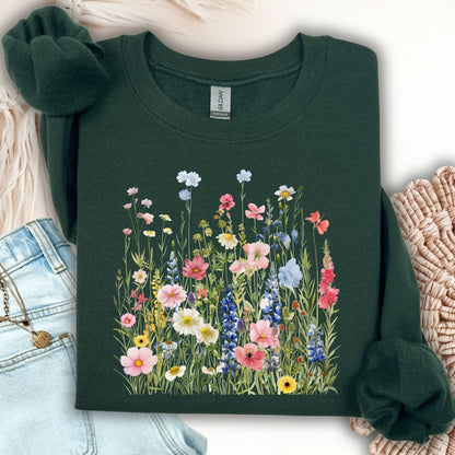 Forest Green Summer Meadow sweatshirt with watercolor wildflowers, folded on a light surface with jeans.