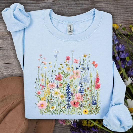 Light blue Summer Meadow sweatshirt with watercolor wildflowers on a rustic wood background.