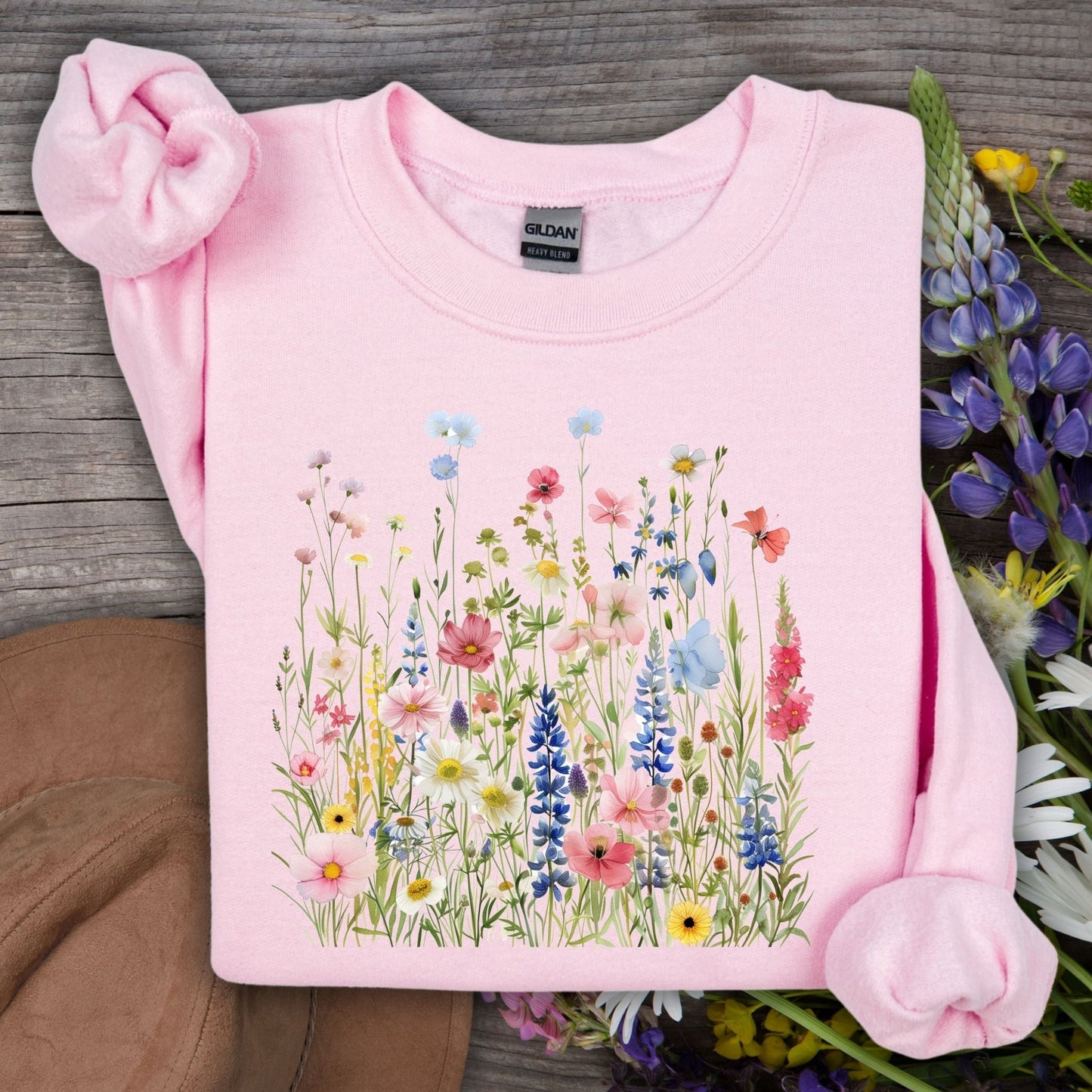 Light pink Summer Meadow sweatshirt with watercolor wildflowers in a rainbow of hues, folded on wood.