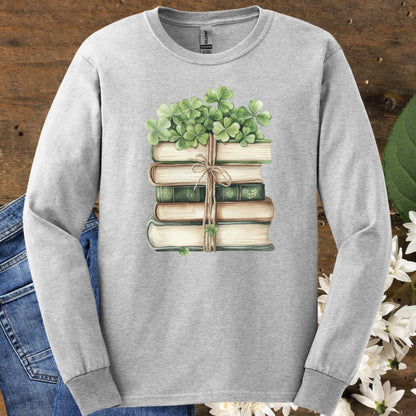 Ash long sleeve tee with a watercolor stack of vintage books tied with twine and topped with four-leaf clovers.